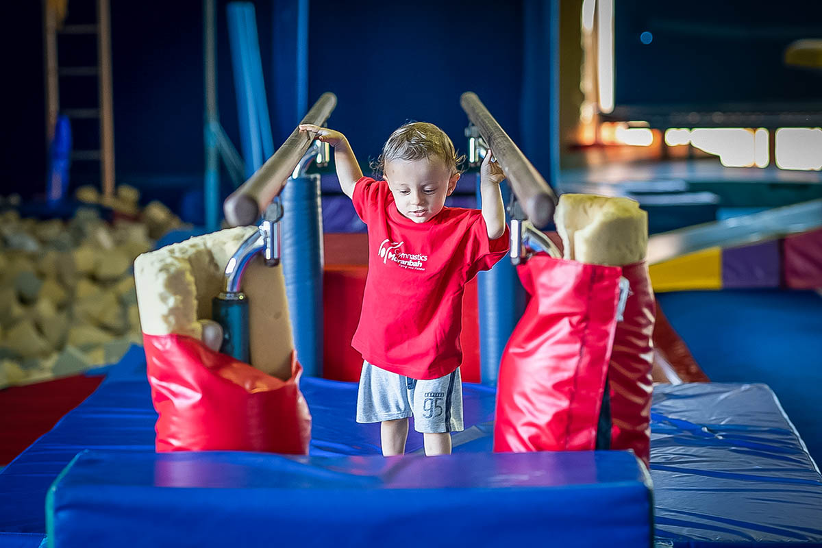 Young boy on gymnastic mat holding bars